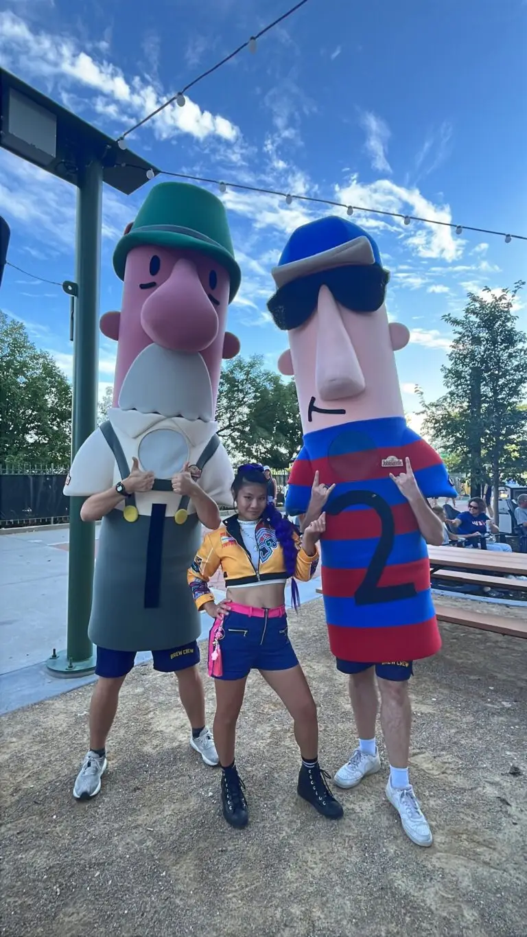 K-Pop dancer posing with two Brewers racing sausage mascots at American Family Field