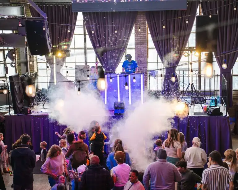 Fog cannons fire in front of the Kid Boogie Down DJ booth as families crowd the stage at a Kid Boogie Down party at The Cooperage.