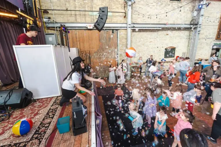 A Kid Boogie Down host kneels at the edge of the stage as kids dance through bubbles and beach balls at The Cooperage in Milwaukee.