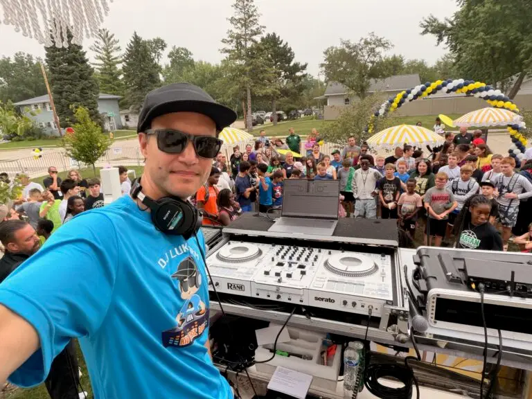 DJ Lukewarm of Kid Boogie Down takes a selfie at the DJ booth with a crowd of students behind him at the Oshkosh Back 2 School Fair